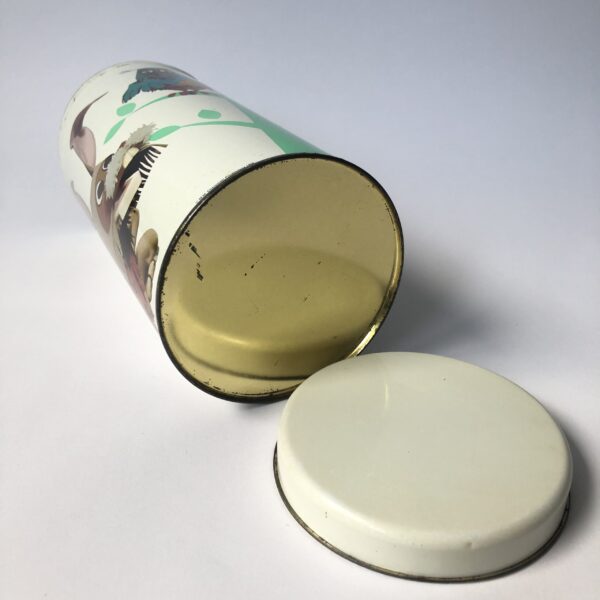 Beschuitbus Fabeltjeskrant uit 1969 - hoogte 22,5 cm - diameter 10,5 cm (3) De Fabeltjeskrant was een populair Nederlands kinderprogramma dat voor het eerst op televisie verscheen in 1968. Het werd bedacht door Leen Valkenier en gemaakt door de Nederlandse televisieproducenten op basis van het idee om een "krant" voor kinderen te creëren met verhalen over dieren in een fantasierijke wereld. De show draaide om de belevenissen van diverse dieren in het dierenbos, die de actualiteit en gebeurtenissen in hun eigen 'wereld' in de vorm van een krant bespraken. De hoofdfiguur was Meneer de Uil, die het nieuws presenteerde en vaak vergezeld werd door andere karakteristieke dieren zoals Juffrouw Ooievaar, Bor de Wolf, en andere kleurrijke figuren. Wat de Fabeltjeskrant bijzonder maakte, was de combinatie van educatieve elementen en humor, evenals de innovatieve manier waarop het gebruikmaakte van poppen en animatie. Het programma was niet alleen geliefd bij kinderen, maar ook bij volwassenen vanwege de scherpe en vaak satirische humor. De show heeft een grote invloed gehad op de Nederlandse kindertelevisie en blijft een nostalgisch icoon voor velen. Na de oorspronkelijke uitzendingen in de jaren '60 en '70, zijn er verschillende pogingen gedaan om het concept nieuw leven in te blazen, waaronder een aantal herhalingen en speciale afleveringen.