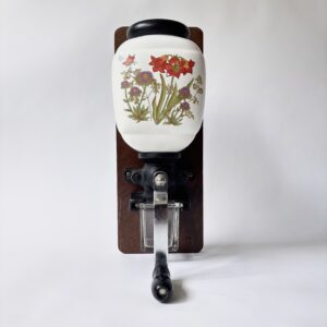 Vintage decoratieve wandkoffiemolen uit de jaren 70 met een porseleinen trechter met bloemmotief en een glazen opvangbakje