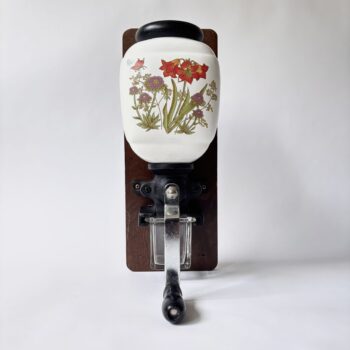 Vintage decoratieve wandkoffiemolen uit de jaren 70 met een porseleinen trechter met bloemmotief en een glazen opvangbakje