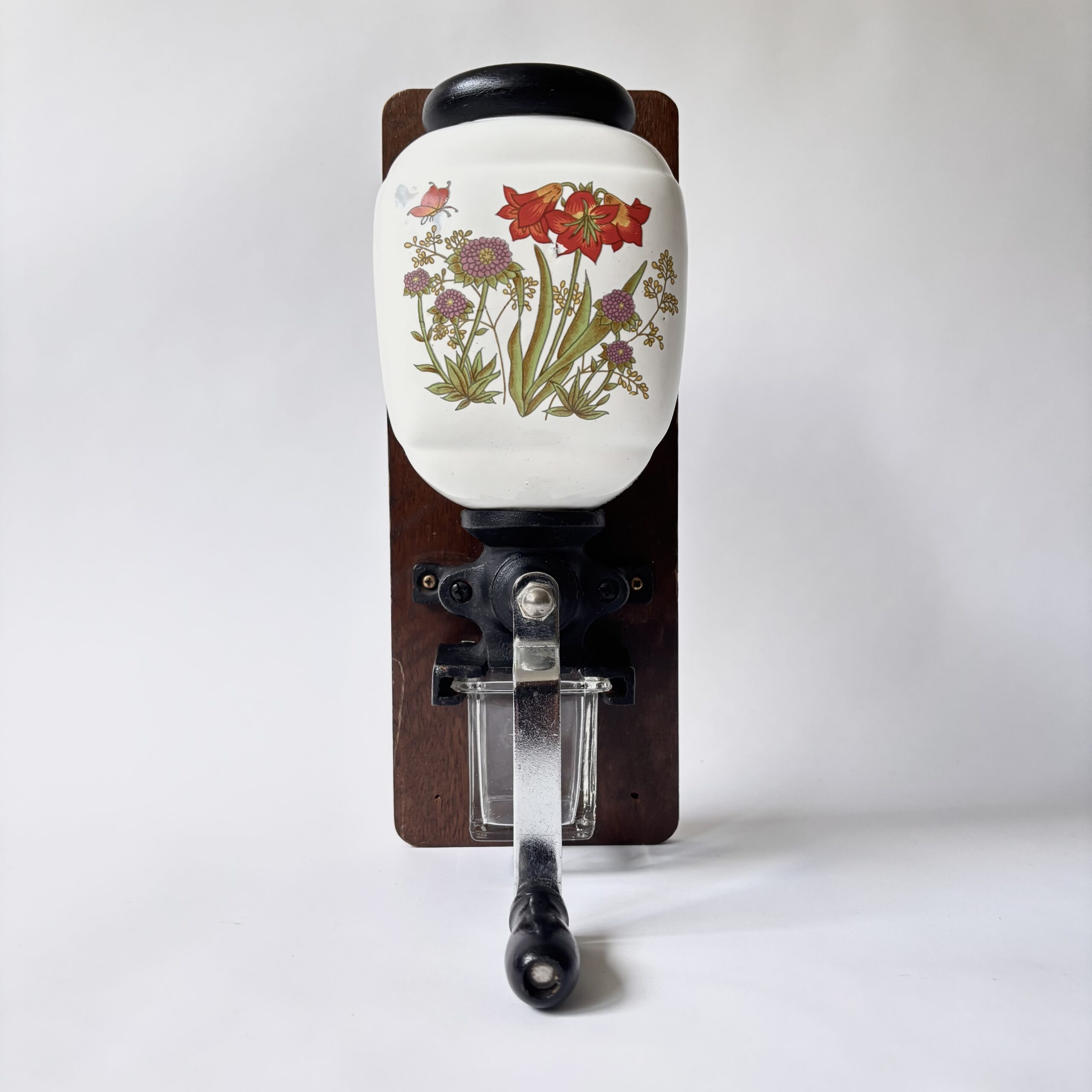 Vintage decoratieve wandkoffiemolen uit de jaren 70 met een porseleinen trechter met bloemmotief en een glazen opvangbakje